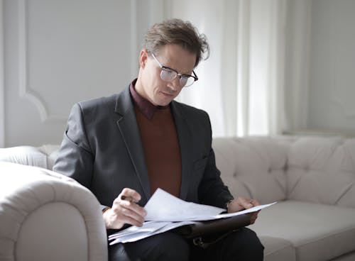 A person in a suit sitting on a sofa and reviewing documents