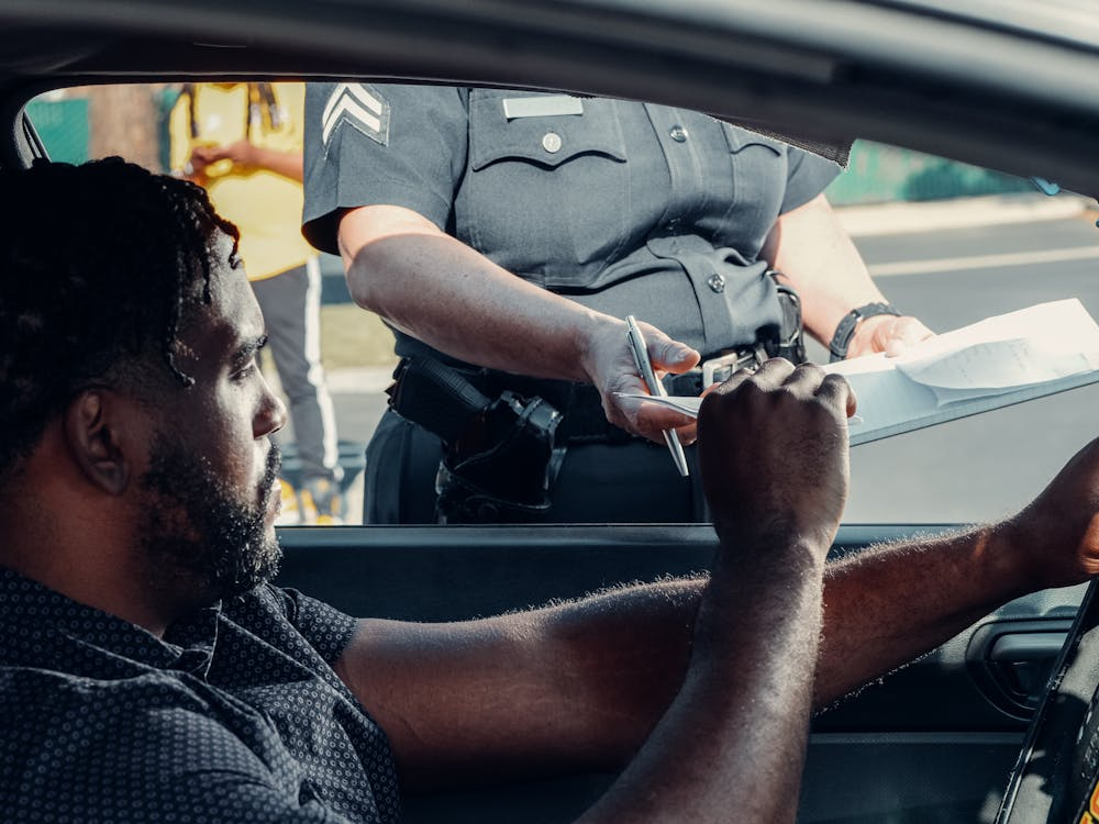 Man sitting inside a car handing a driver’s license to a police officer during a traffic stop in New Jersey